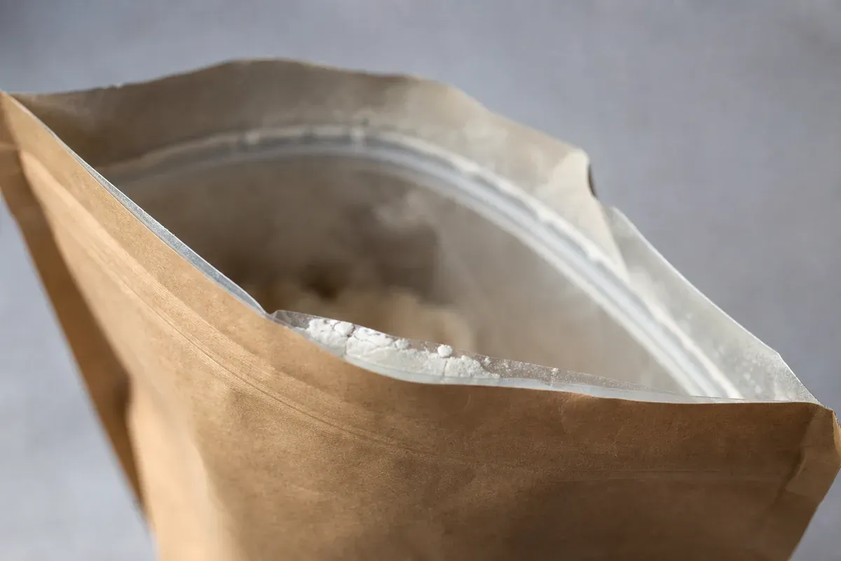 Gros plan sur la fermeture zip refermable en haut d'un sachet de whey protéine, partiellement ouverte et déformée